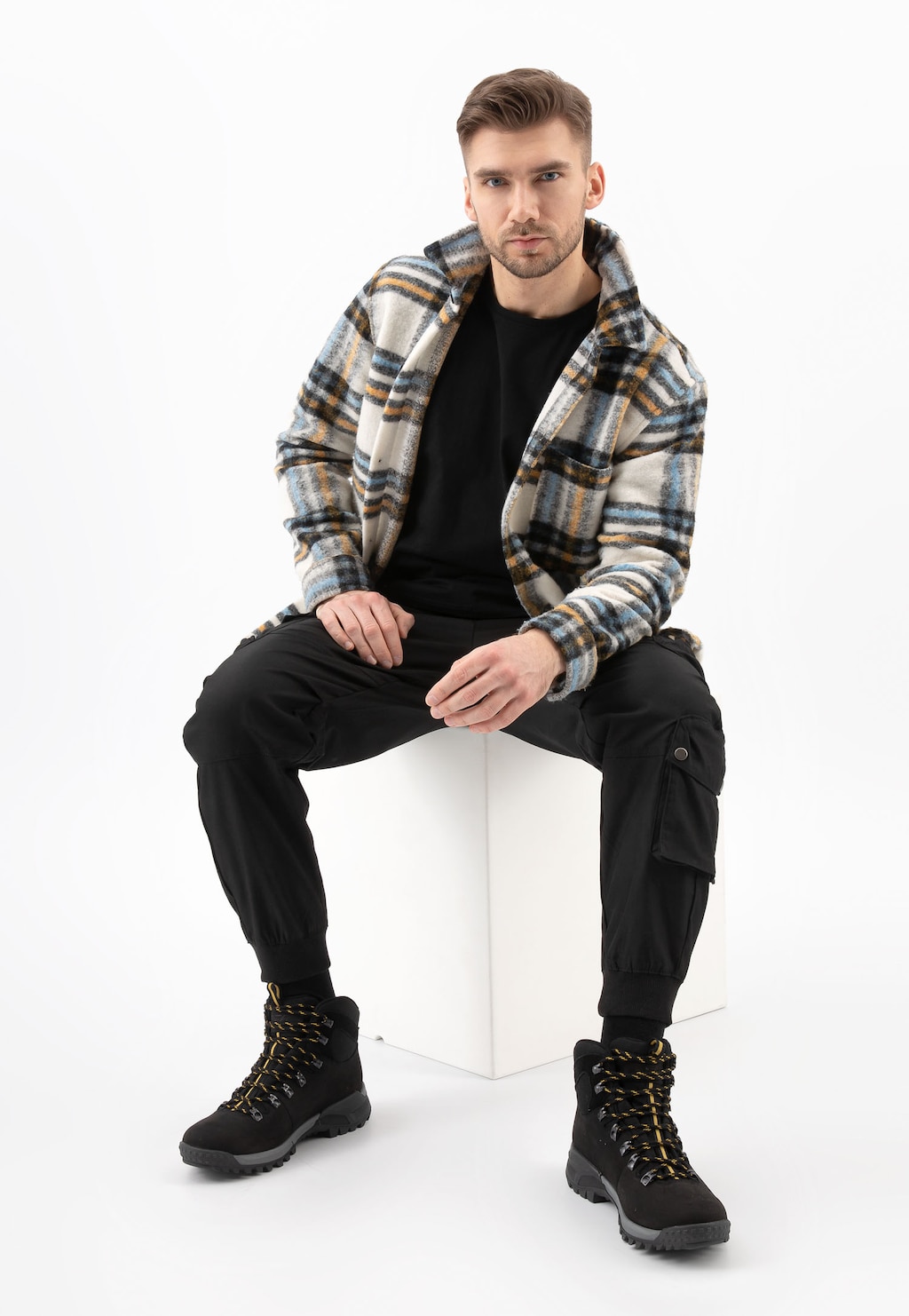 Mężczyzna w kraciastej koszuli siedzi na białym stołku, prezentując czarne trzewiki trekkingowe Wojas 24028-71 wykonane z łączonych materiałów, idealne do stylizacji outdoorowych.