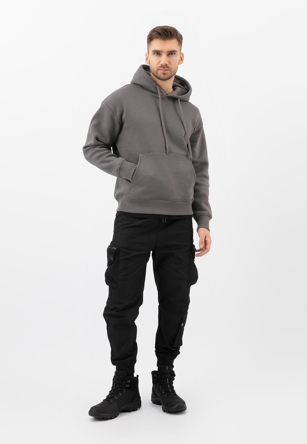 Mężczyzna w szarej bluzie z kapturem i czarnych spodniach cargo, prezentujący czarne wysokie trzewiki trekkingowe Wojas model 24029-71.