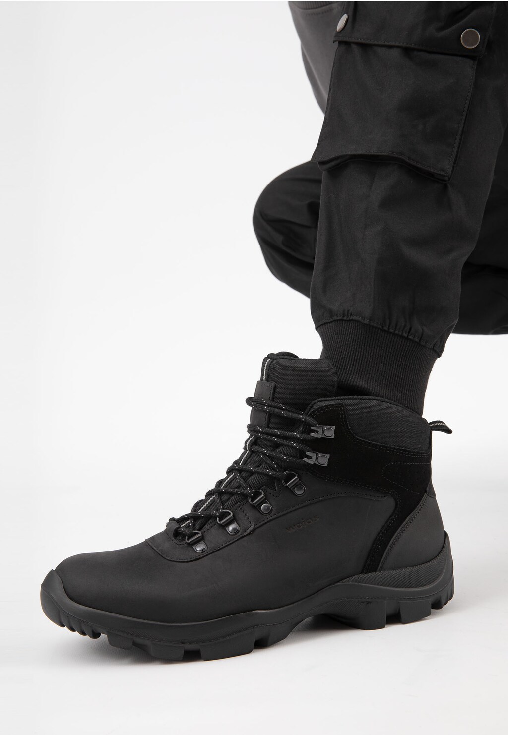 Czarne wysokie trzewiki trekkingowe Wojas model 24029-71 prezentowane na nodze w ciemnych spodniach, widok z boku ukazujący masywną podeszwę i sznurowanie.