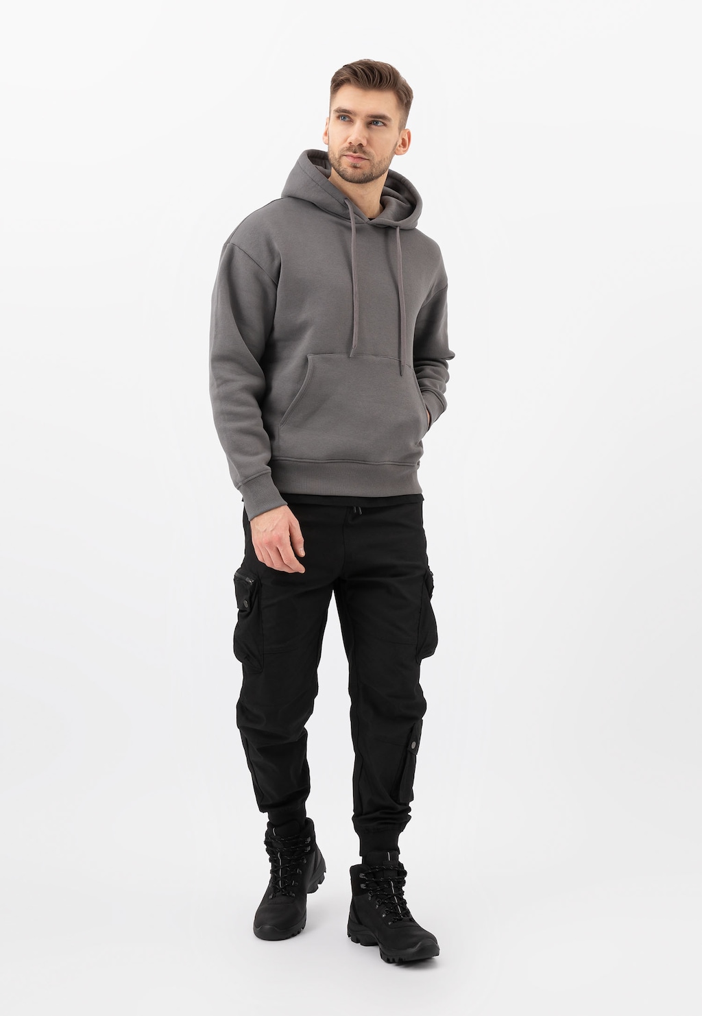 Mężczyzna w szarej bluzie z kapturem i czarnych spodniach cargo, prezentujący czarne wysokie trzewiki trekkingowe Wojas model 24029-71 w pełnej stylizacji.
