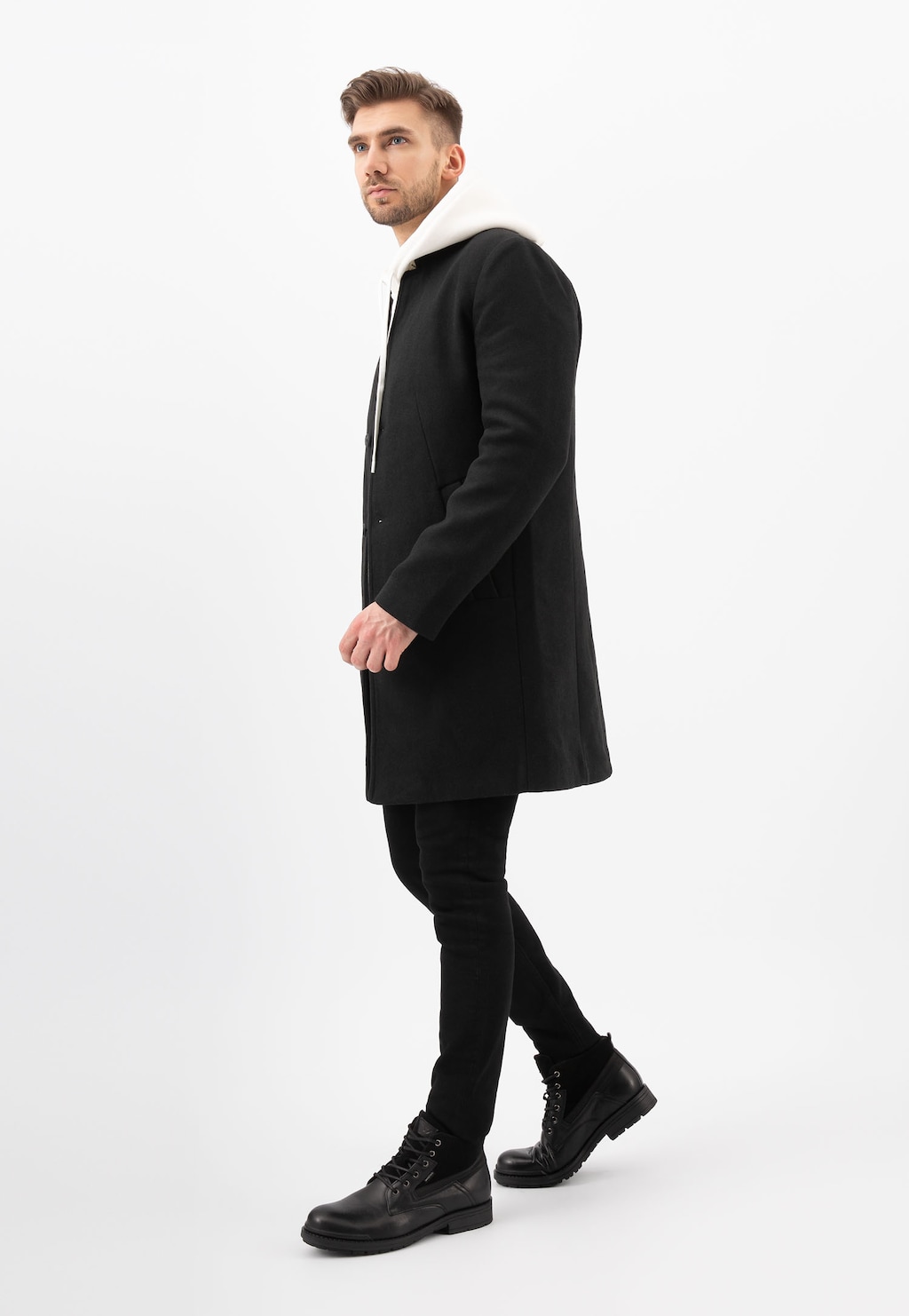 Elegancki mężczyzna w czarnym płaszczu i spodniach, prezentujący czarne ocieplane trzewiki męskie Wojas model 24033-71 typu workery, ukazane w profilu podczas chodzenia.