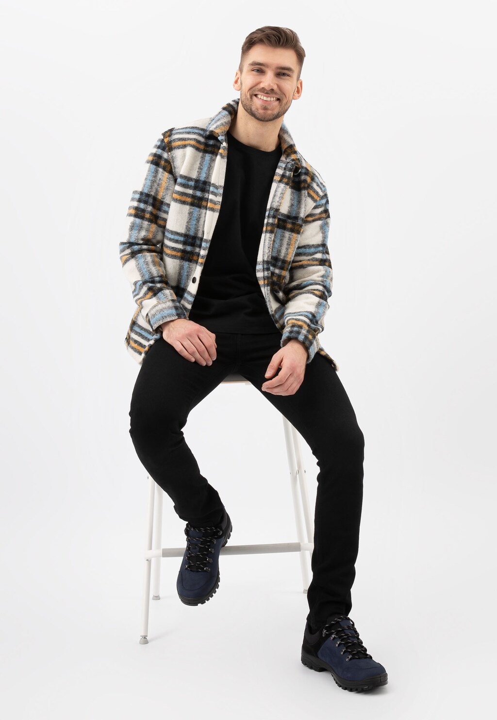 Mężczyzna w kraciastej koszuli siedzi na stołku, prezentując czarno-granatowe półbuty trekkingowe Wojas model 10068-96 w połączeniu z codziennym strojem.