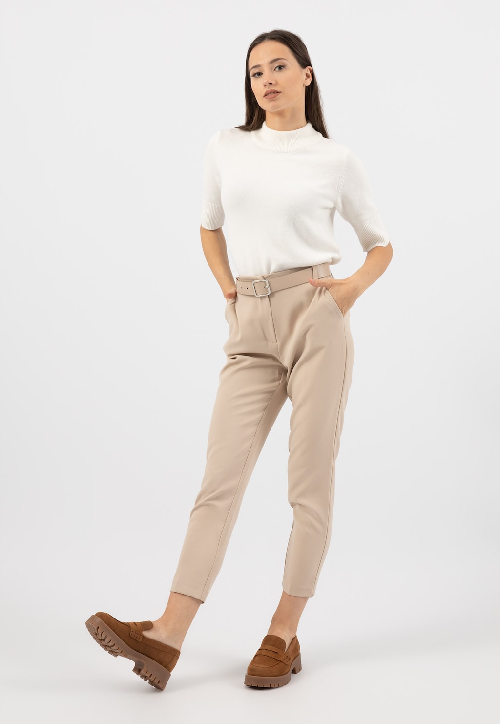 Modelka w eleganckiej stylizacji prezentująca jasnobrązowe mokasyny Wojas model 46124-63 z dwoiny welurowej, noszone do białej bluzki i beżowych spodni.