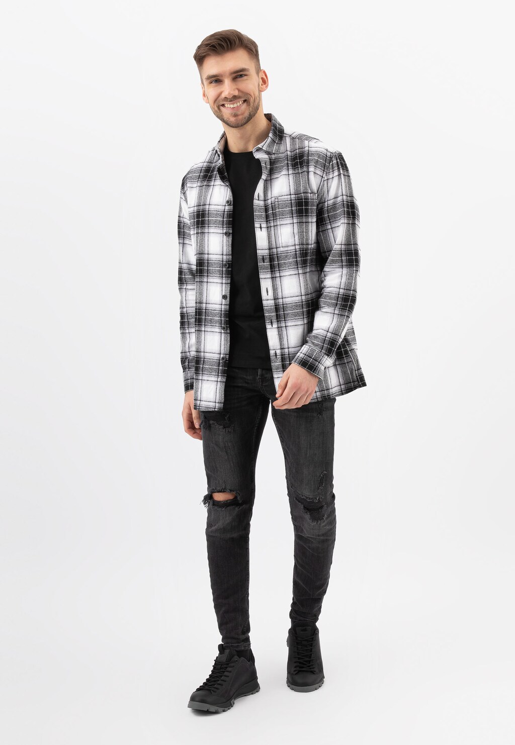 Model w czarno-białej koszuli w kratę i czarnych spodniach, prezentujący czarne sznurowane półbuty trekkingowe Wojas 10139-71.