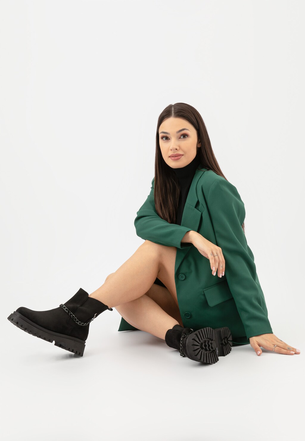 Kobieta w zielonej marynarce prezentująca czarne sztyblety Wojas 55183-61 z dwoiny welurowej, z widocznym ozdobnym łańcuchem, ukazujące modny, miejski styl obuwia.