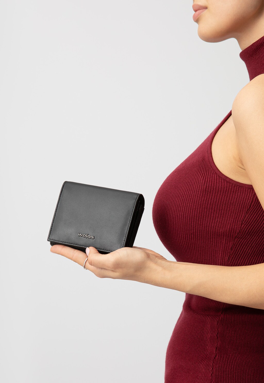 Czarny klasyczny portfel damski Wojas model 91051-51 z licowej skóry trzymany w dłoni przez osobę w bordowej sukience z golfem, prezentowany z boku.
