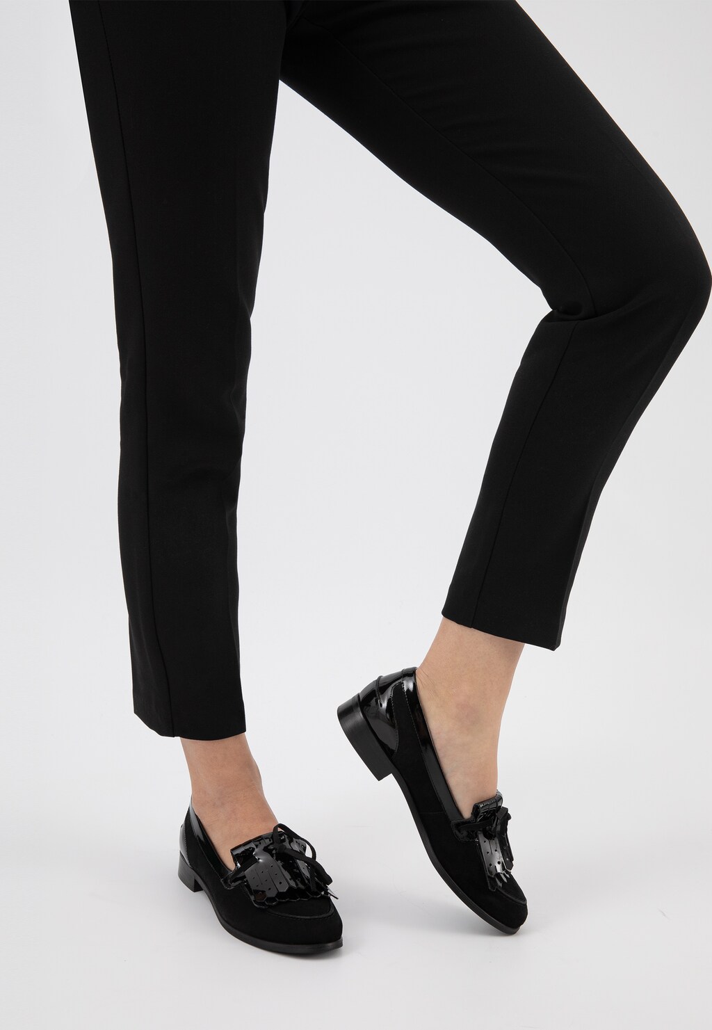 Eleganckie wsuwane półbuty damskie Wojas model 9411-71 w kolorze czarnym, noszone z czarnymi spodniami. Widok z boku podkreśla klasyczny design i niski obcas.