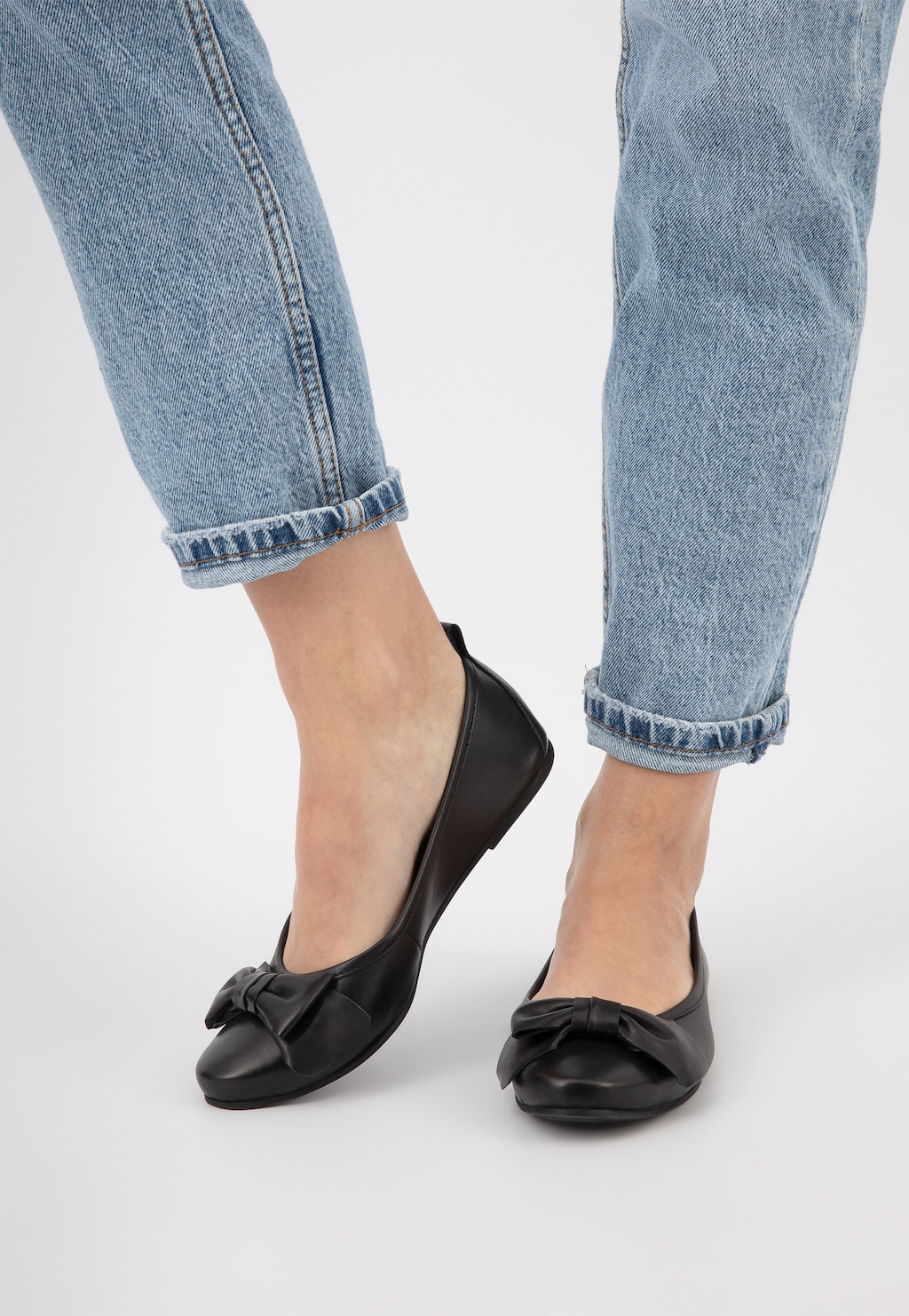 Czarne eleganckie baleriny Wojas 44007-51 ze skóry licowej z ozdobną kokardką, prezentowane na nogach w jasnoniebieskich jeansach, widok z przodu.