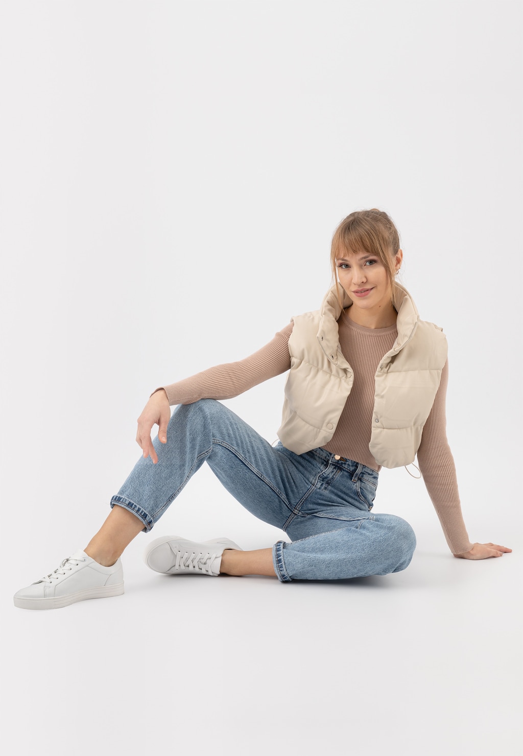 Białe trampki damskie Wojas model 46019-59 ze skóry licowej prezentowane na modelce w beżowym swetrze, puchowej kamizelce i jeansach, w casualowej pozycji siedzącej.
