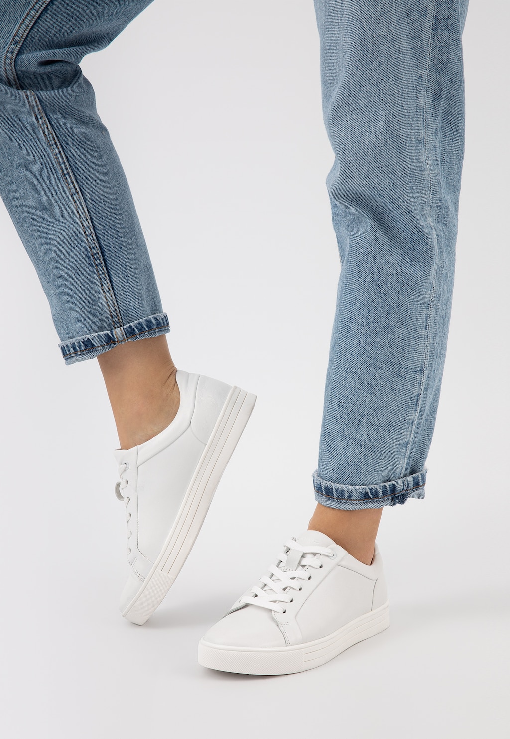 Białe trampki damskie Wojas model 46019-59 ze skóry licowej na nodze osoby w niebieskich jeansach, ukazujące minimalistyczny design i codzienną elegancję.