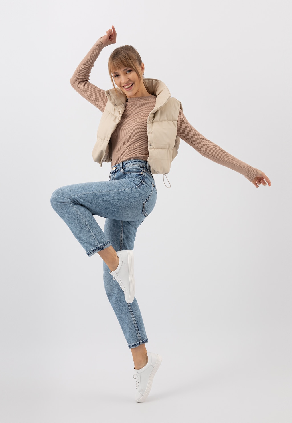 Kobieta w białych trampkach Wojas model 46019-59 ze skóry licowej, ubrana w beżową kamizelkę i jeansy, w dynamicznej pozie z uniesioną nogą.