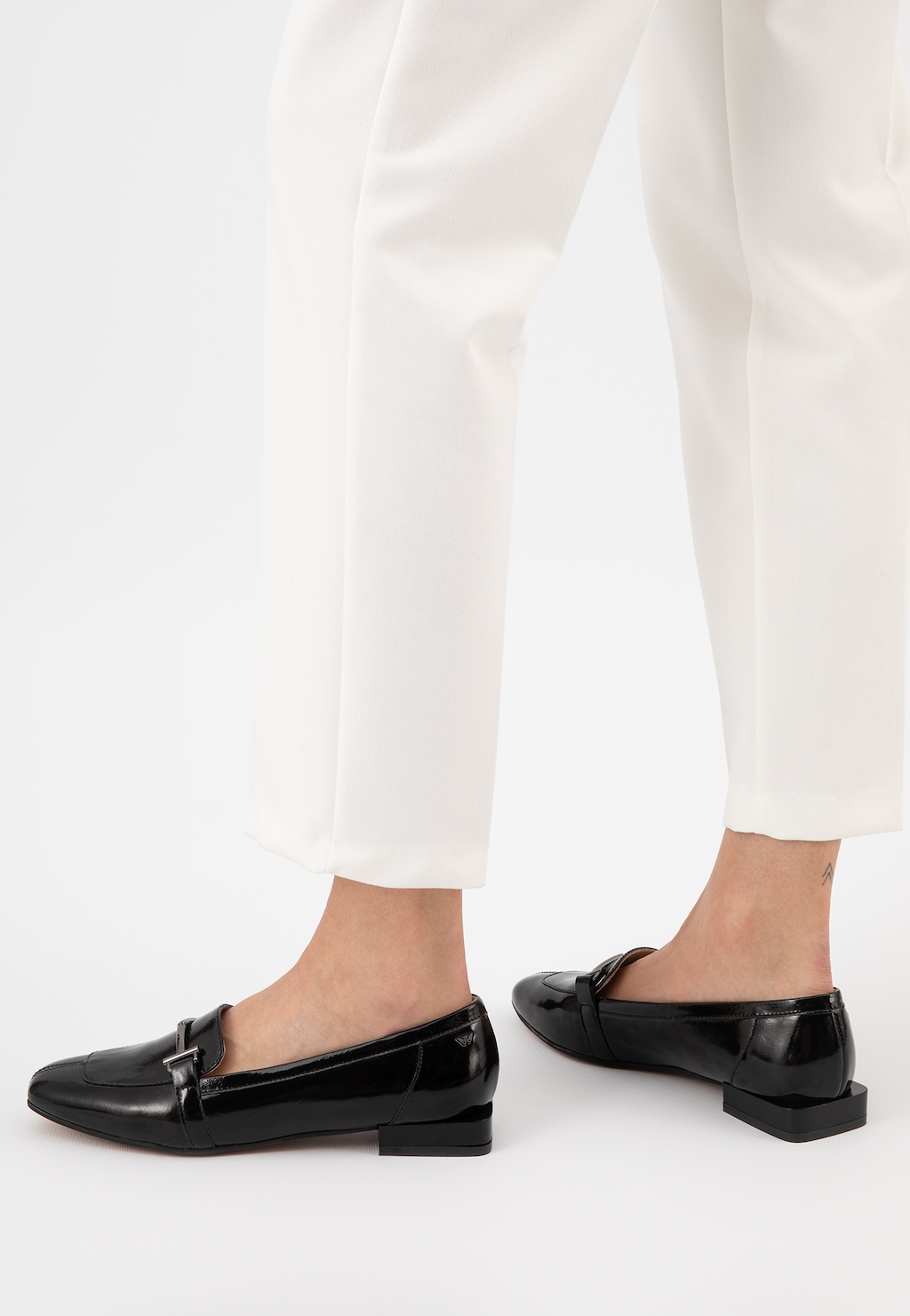 Czarne lakierowane mokasyny damskie Wojas model 46223-31 z metalową ozdobą, prezentowane na nogach w białych spodniach, widok z boku.