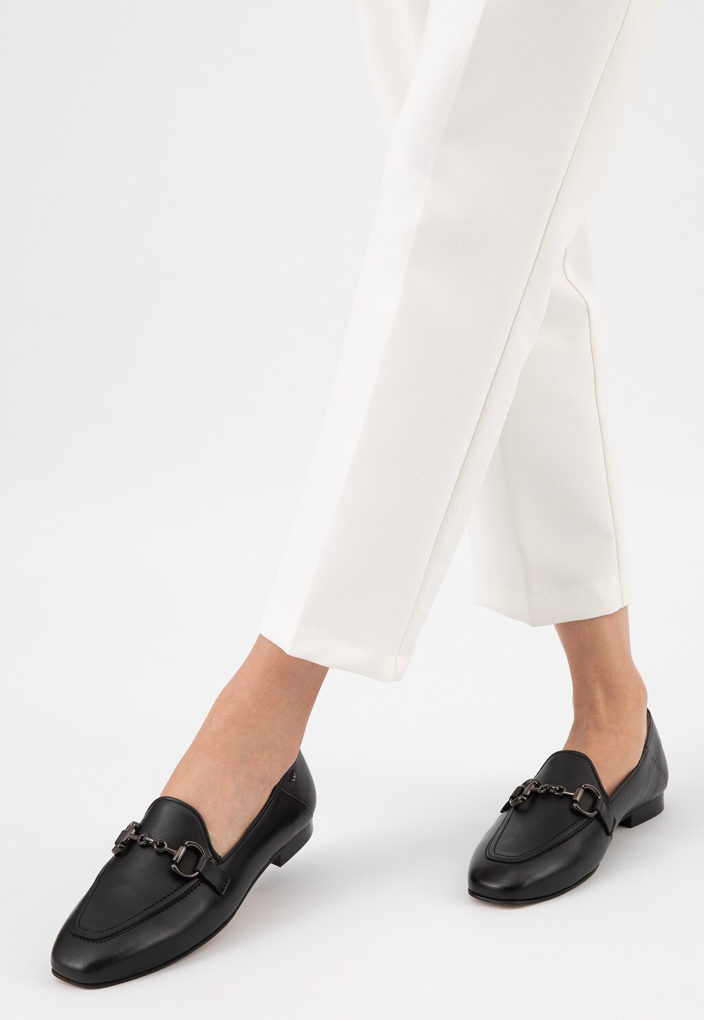 Eleganckie czarne skórzane półbuty damskie Wojas model 46224-51 z metalową ozdobą na przodzie, prezentowane na nogach osoby ubranej w białe spodnie.