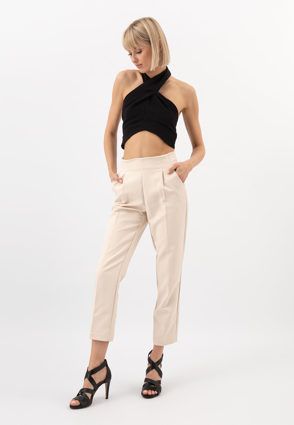 Modelka w czarnym topie i jasnych spodniach prezentuje czarne sandały damskie Wojas na szpilce model 76045-51 z krzyżowymi paskami.