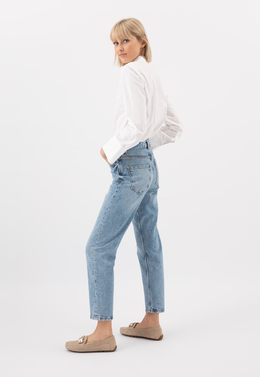 Kobieta w białej koszuli i jeansach, nosząca beżowe mokasyny damskie Wojas model 46208-64 z ozdobnymi kryształami, ukazana z profilu.