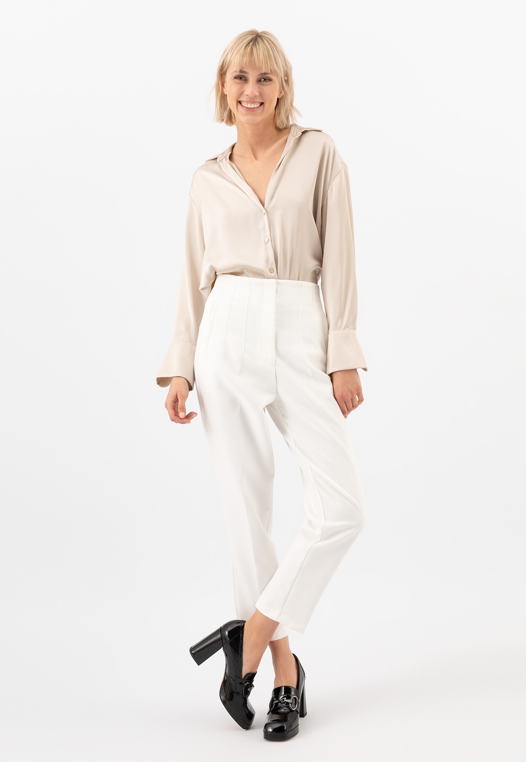 Kobieta w eleganckim stroju prezentująca wysokie lakierowane mokasyny damskie Wojas na słupku model 46216-31, idealnie dopasowane do białych spodni i beżowej koszuli.