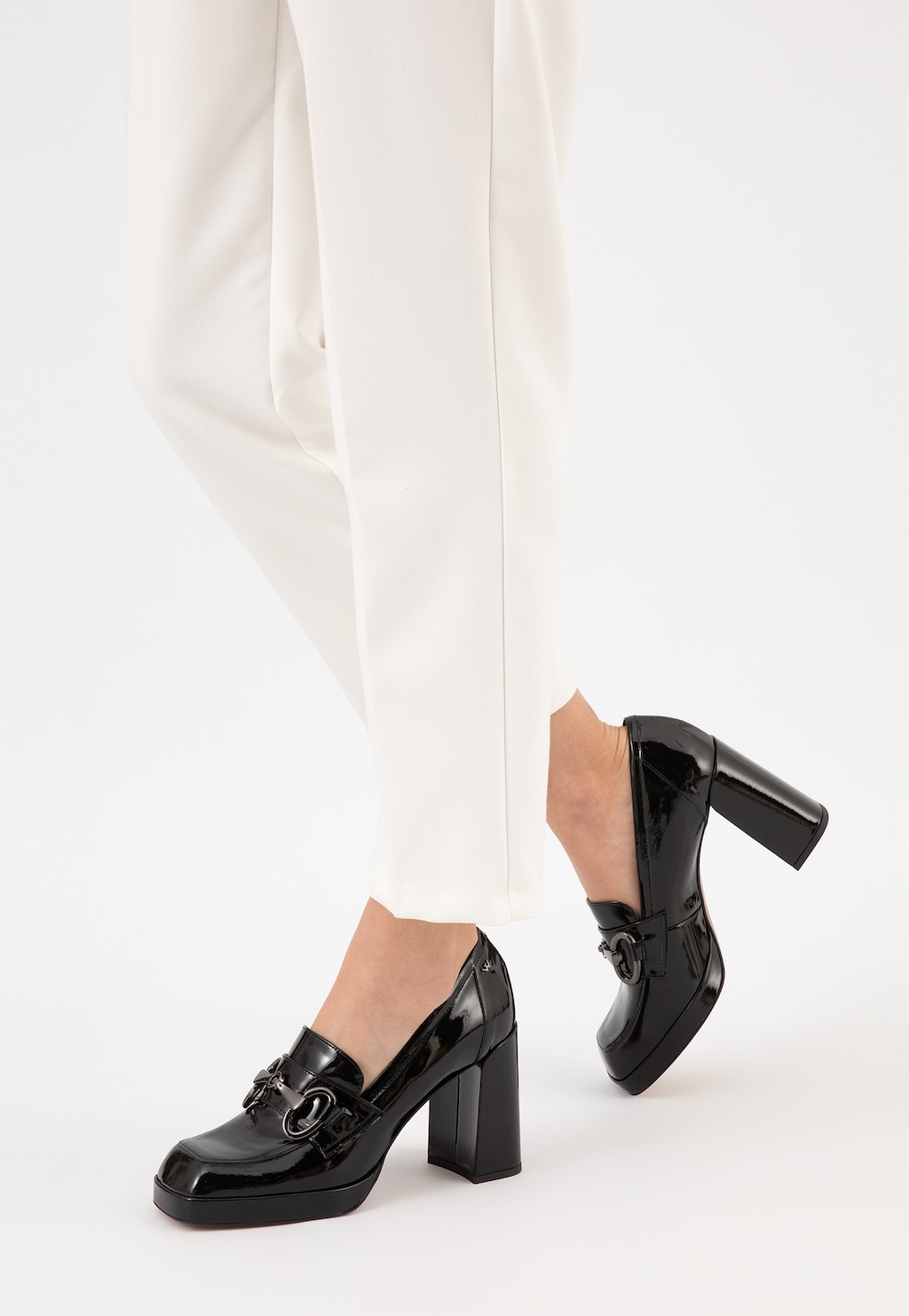 Eleganckie czarne lakierowane mokasyny damskie Wojas 46216-31 na solidnym słupku, noszone do białych spodni, widoczne z profilu podkreślające stylowy charakter obuwia.
