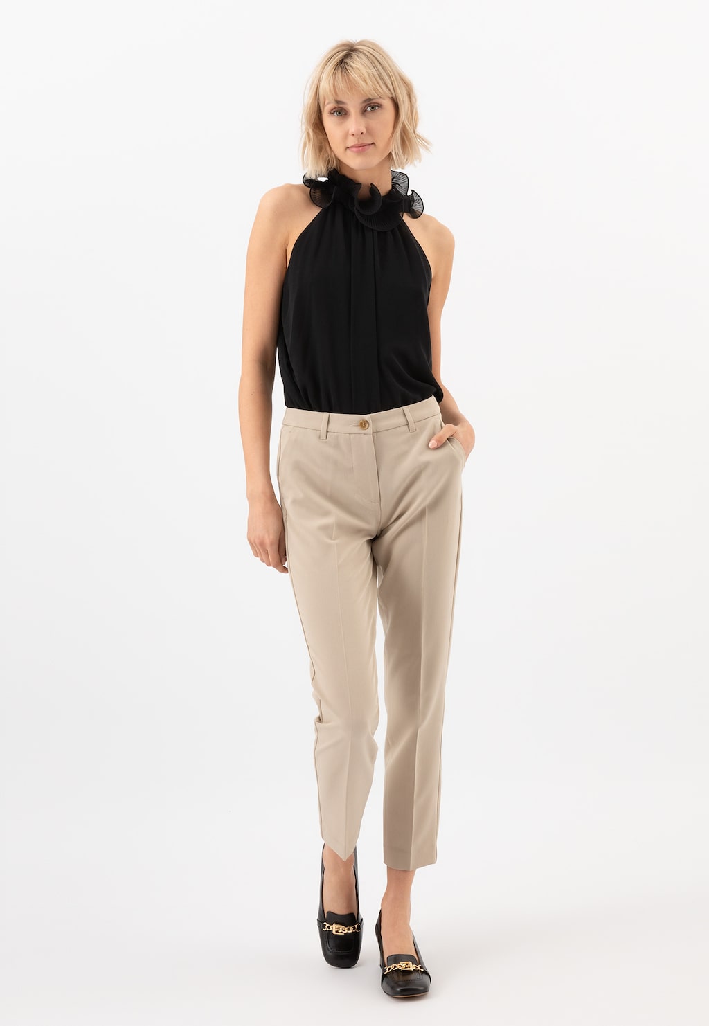 Elegancka stylizacja z czarną halterneck bluzką i beżowymi spodniami, uzupełniona czarnymi mokaszynami Wojas 46237-51 z charakterystyczną złotą ozdobą na obcasie.