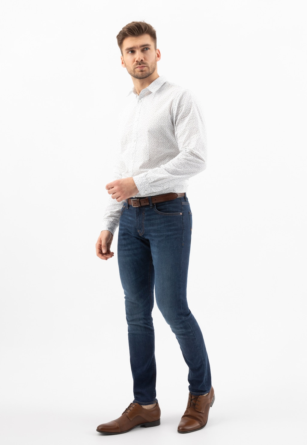 Model w eleganckiej stylizacji prezentuje brązowe półbuty męskie Wojas 9036-52 w połączeniu z białą koszulą i granatowymi jeansami.