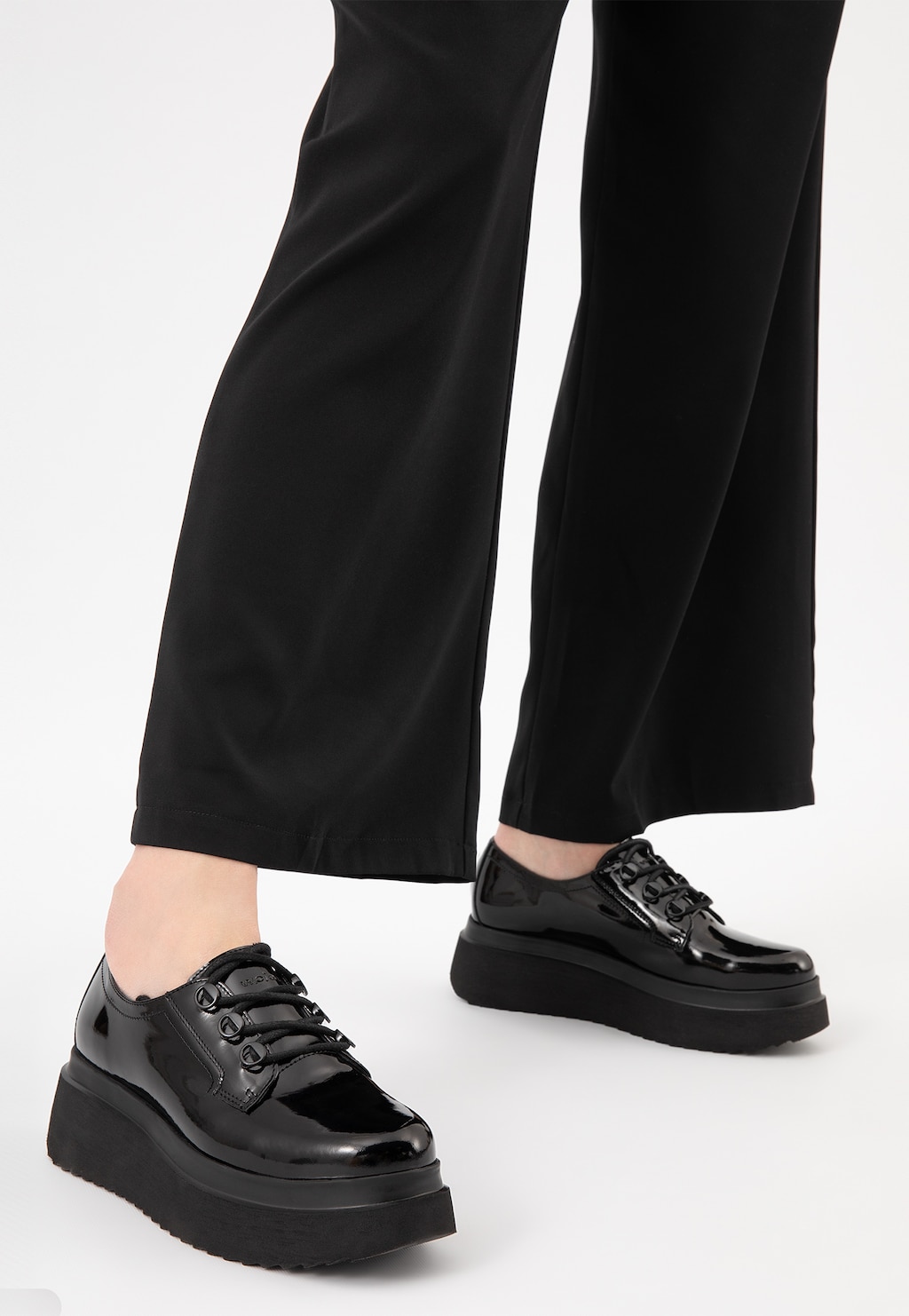 Czarne creepersy damskie Wojas model 46006-39 z lakierowanej skóry na grubej platformie, prezentowane na nogach osoby w czarnych, szerokich spodniach.