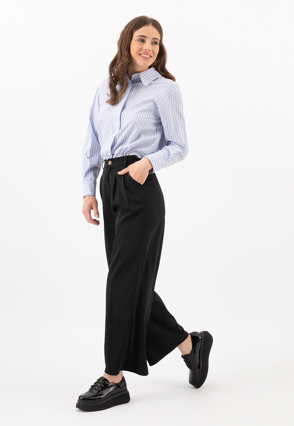 Modelka w eleganckim stroju z błękitną koszulą w paski i szerokimi czarnymi spodniami, prezentująca czarne creepersy Wojas z lakierowanej skóry model 46006-39 na grubej podeszwie.