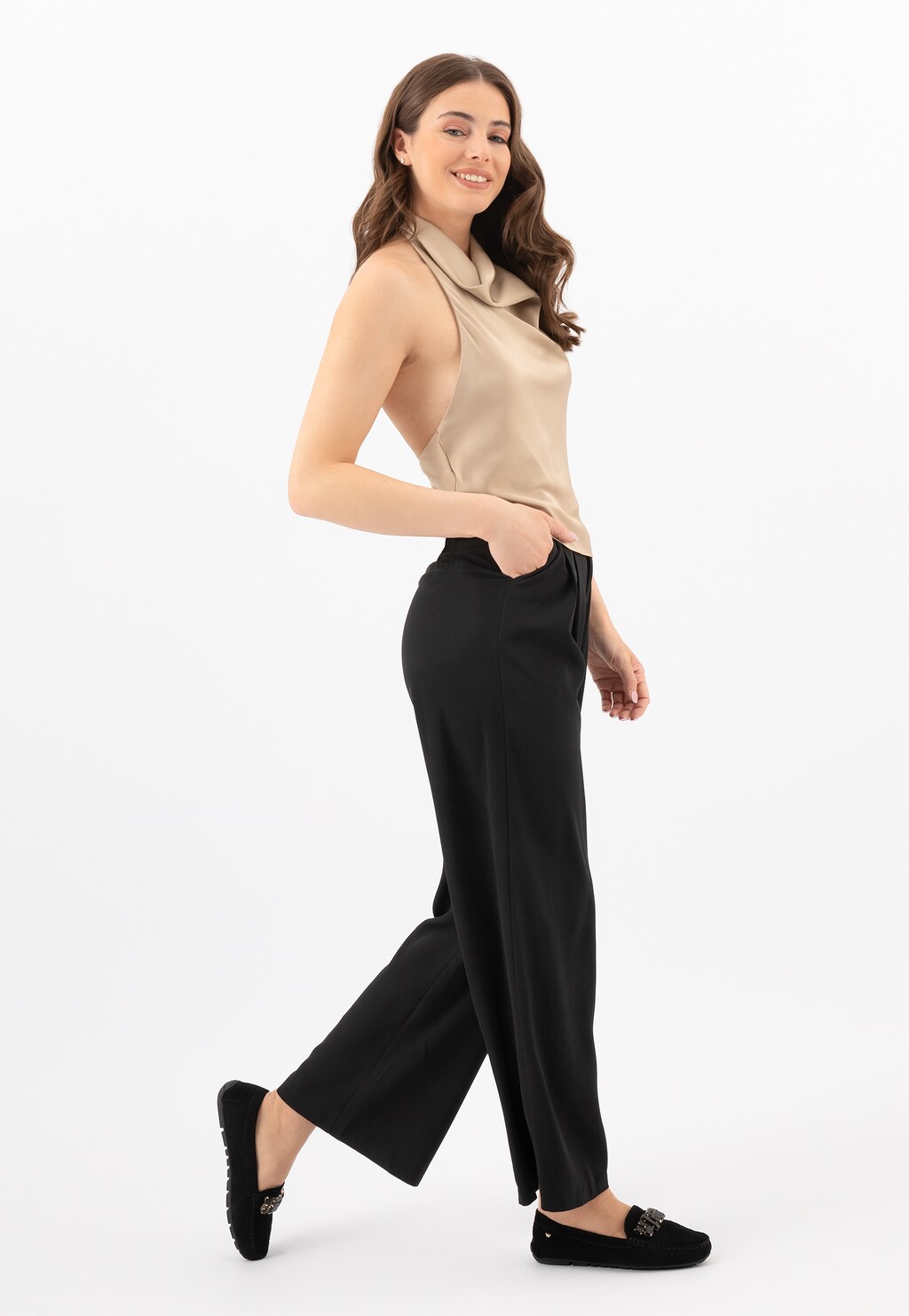 Modelka w beżowej bluzce i czarnych spodniach prezentuje czarne mokasyny damskie Wojas model 46208-61 z elegancką kryształową aplikacją, idealne do stylizacji biznesowej.