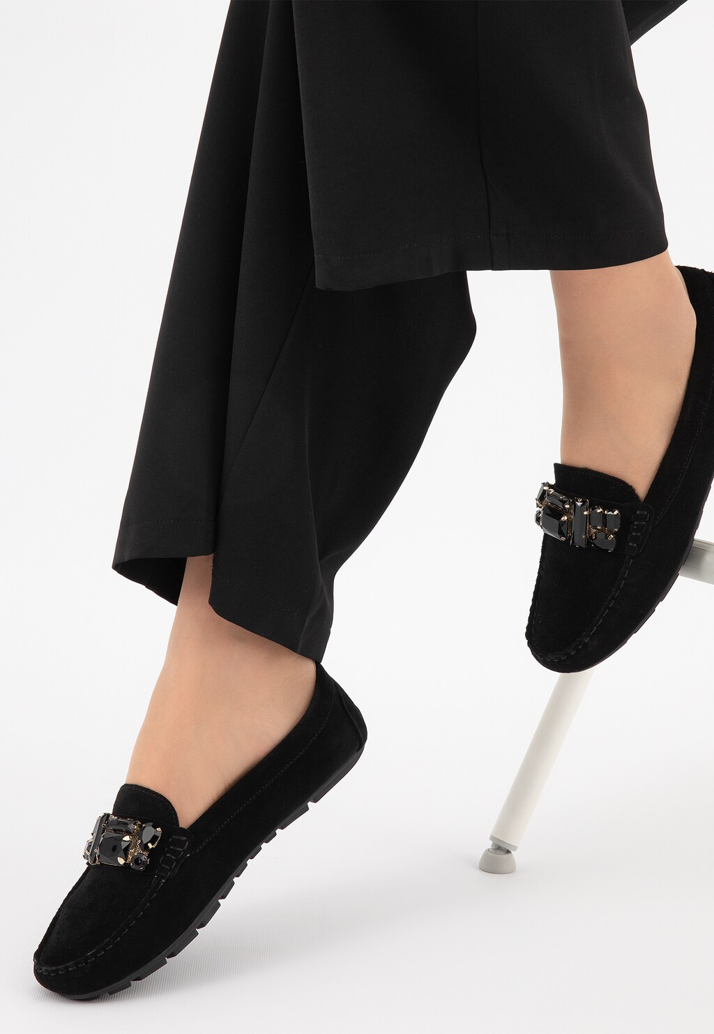 Czarne mokasyny damskie Wojas 46208-61 z kryształową aplikacją na przodzie, prezentowane na nogach kobiety w czarnych spodniach, eleganckie i wygodne obuwie na co dzień.
