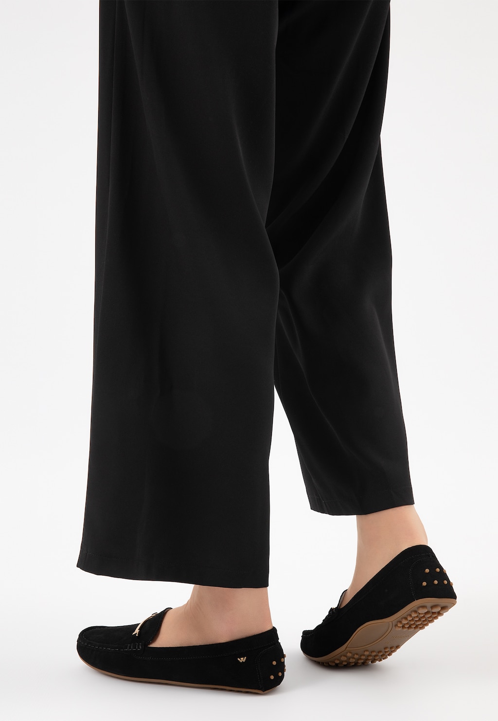 Eleganckie czarne mokasyny damskie Wojas model 46210-61 typu car shoes z gumową podeszwą, widoczne na nodze w czarnych spodniach, ujęcie z perspektywy tyłu.