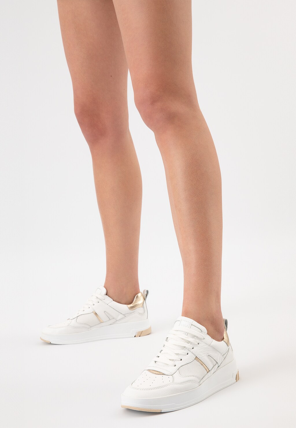 Białe skórzane trampki damskie Wojas model 46211-79 ze złotymi akcentami, prezentowane na nogach modelki, nowoczesny sportowy design z eleganckim wykończeniem.