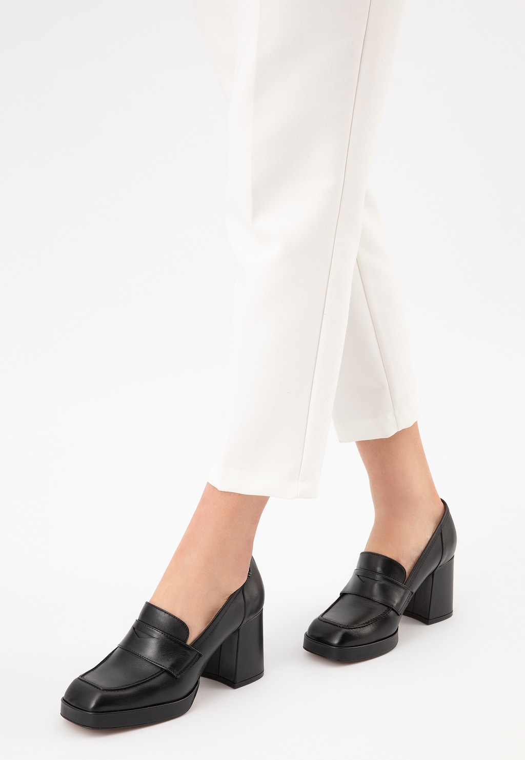 Czarne skórzane mokasyny damskie Wojas 46219-51 z kwadratowym noskiem i wysokim obcasem, eksponowane na nogach modelki w białych spodniach.