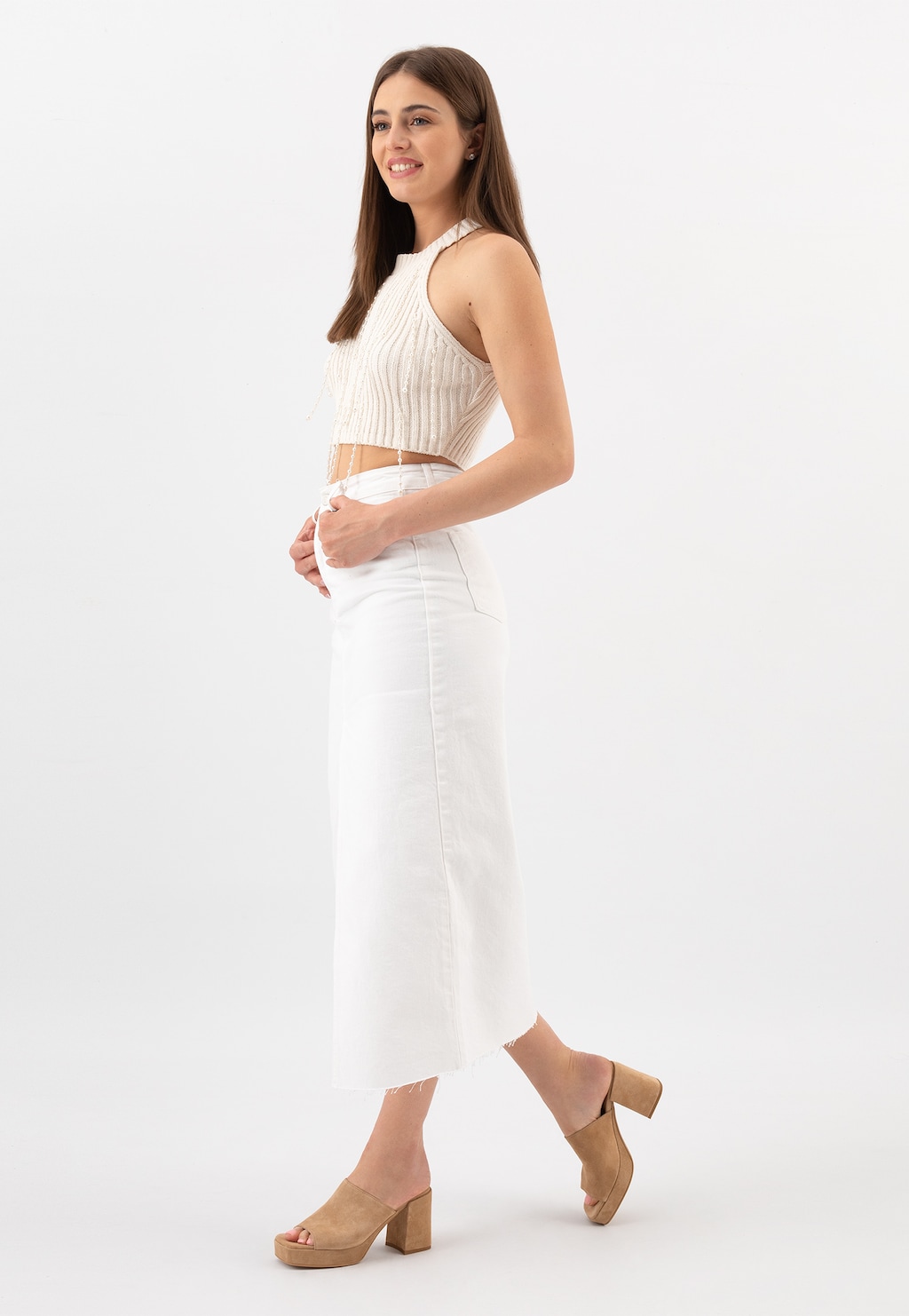 Modelka w białym komplecie z beżowymi klapkami Wojas na słupku model 74036-64, ukazane z profilu. Elegancki look uzupełniają buty o modnym fasonie i wygodnej wysokości obcasa.