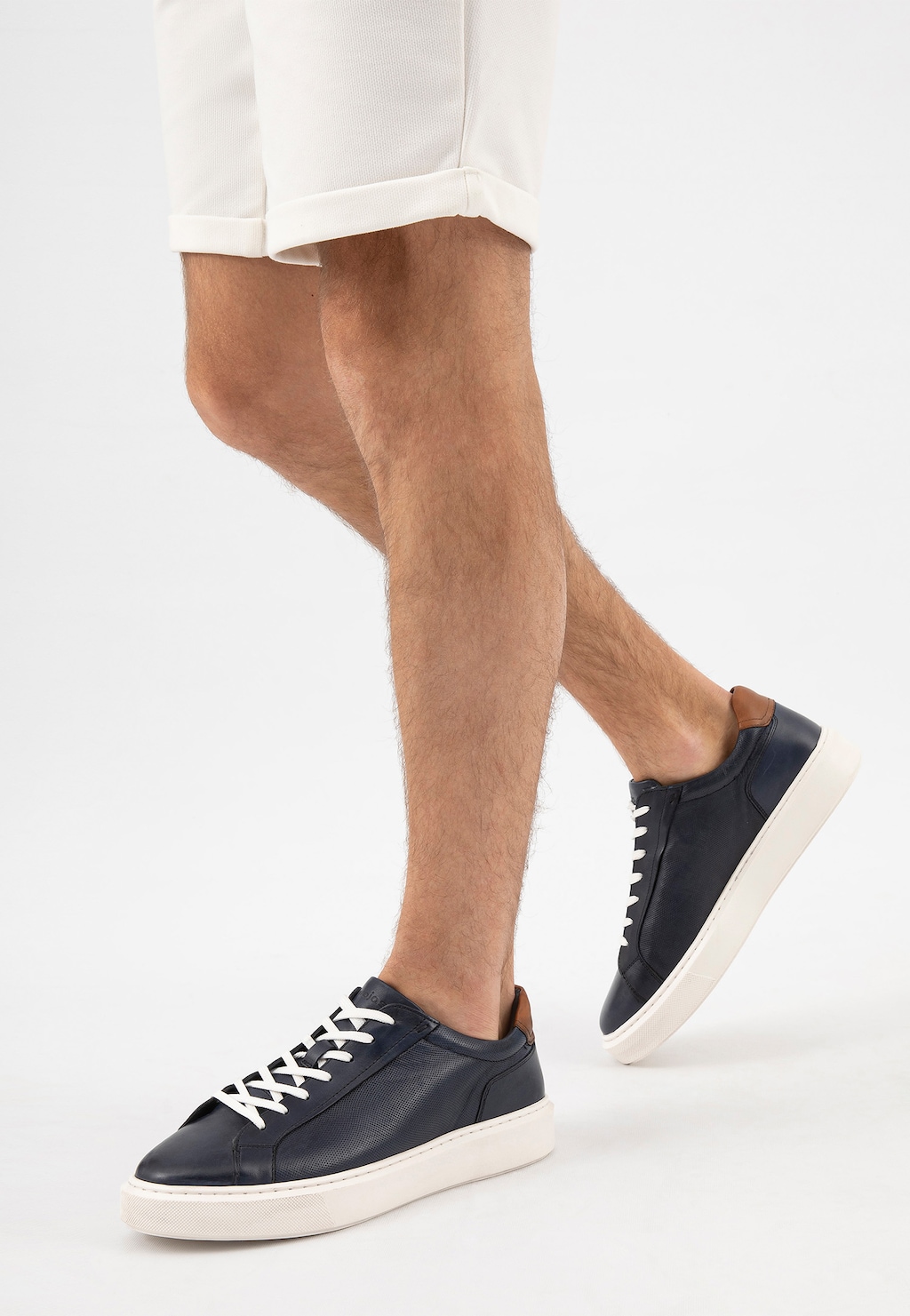 Granatowe trampki męskie Wojas 10160-56 ze skóry licowej z brązowymi wstawkami, białymi sznurówkami i podeszwą, na nogach modela w białych szortach.