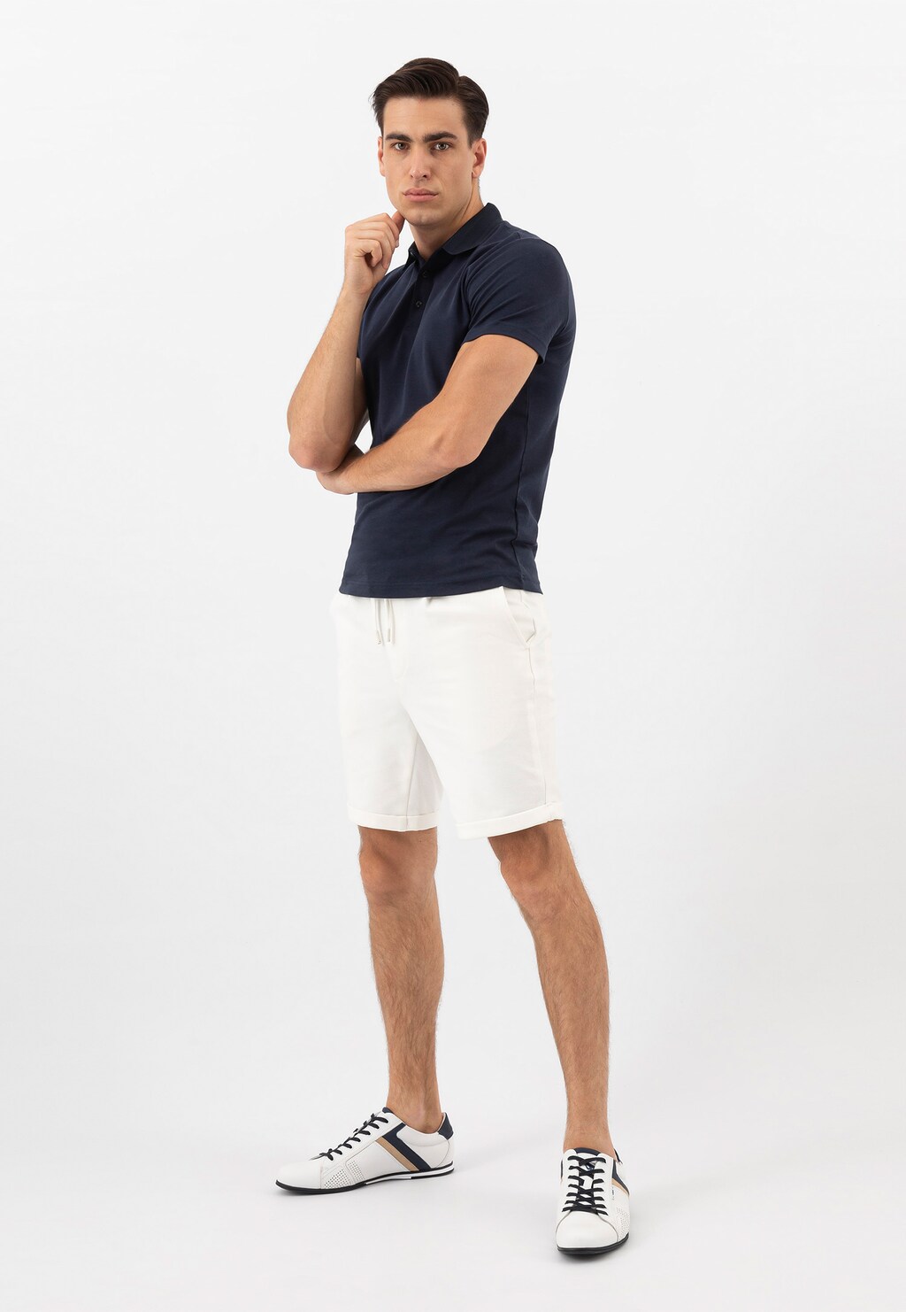 Stylizacja męska z granatową koszulką polo i białymi szortami, uzupełniona białymi skórzanymi sneakersami Wojas 10157-79 z granatowymi i beżowymi akcentami.
