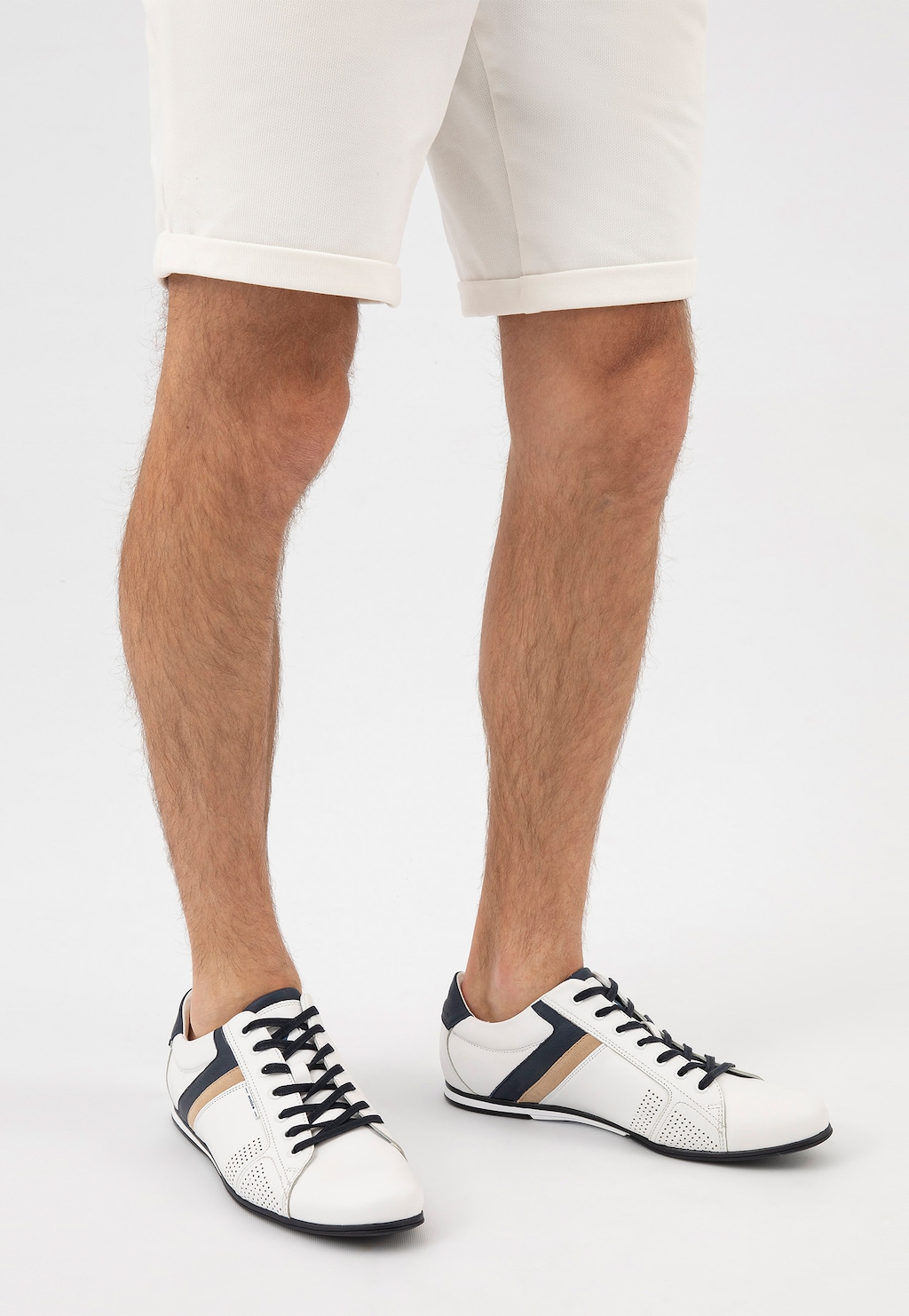 Białe skórzane sneakersy Wojas 10157-79 z granatowymi i beżowymi akcentami na nogach mężczyzny w kremowych krótkich spodniach, widok z przodu butów.