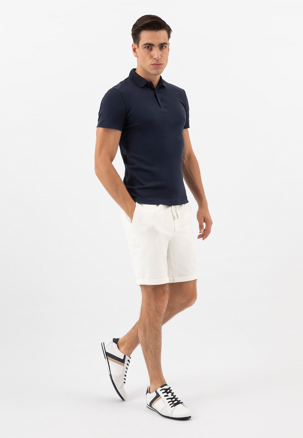 Model w granatowej koszulce polo i białych szortach, prezentujący białe skórzane sneakersy Wojas 10157-79 z granatowymi i beżowymi elementami, widoczne w dynamicznej pozie.