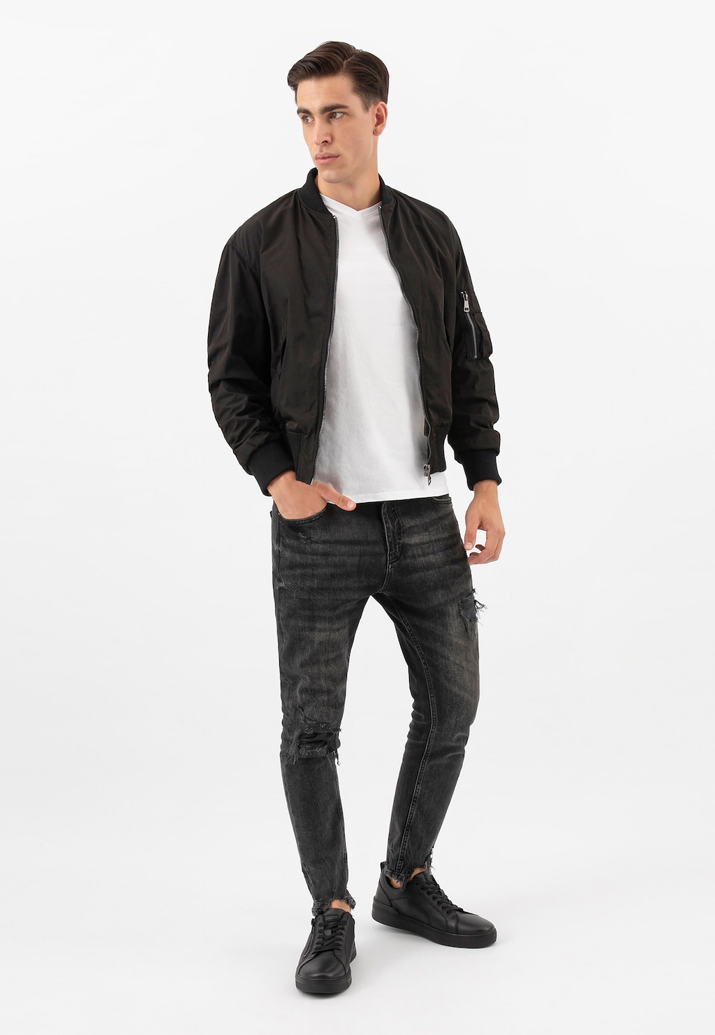 Model w czarnej kurtce typu bomber, białej koszulce i czarnych jeansach, prezentujący czarne trampki Wojas 10149-51 ze skóry licowej z zamkiem na cholewce.