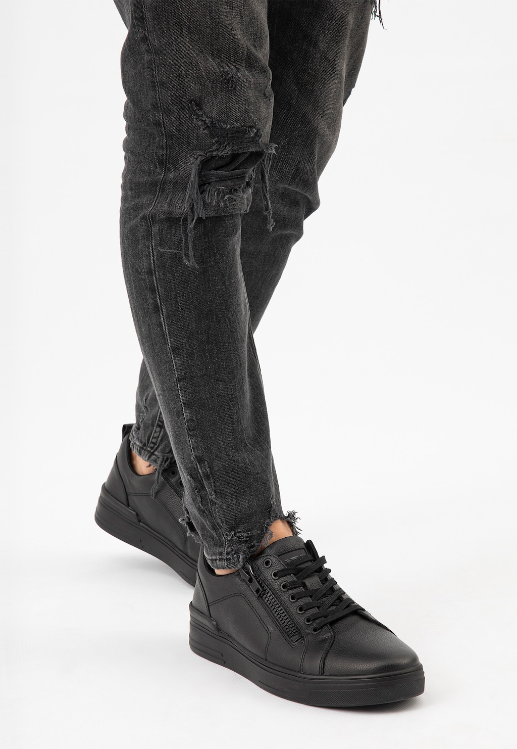Czarne trampki Wojas model 10149-51 ze skóry licowej z bocznym zamkiem, noszone z poszarpanymi jeansami, widok z perspektywy nóg.
