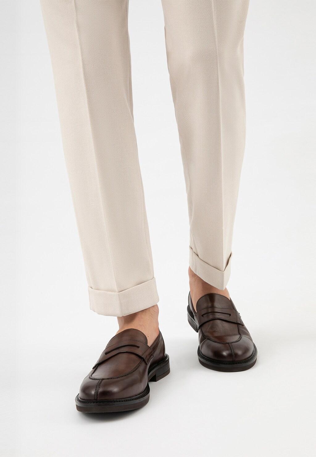 Brązowe mokasyny męskie Wojas model 10137-52 ze skóry licowej na nogach mężczyzny w jasnych, eleganckich spodniach z podwiniętymi nogawkami.