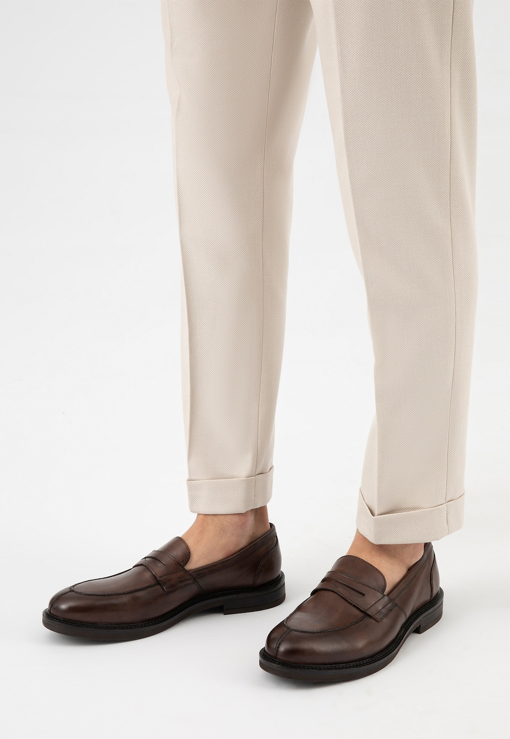 Brązowe mokasyny męskie Wojas model 10137-52 ze skóry licowej prezentowane na nogach w jasnych eleganckich spodniach z podwiniętymi nogawkami.