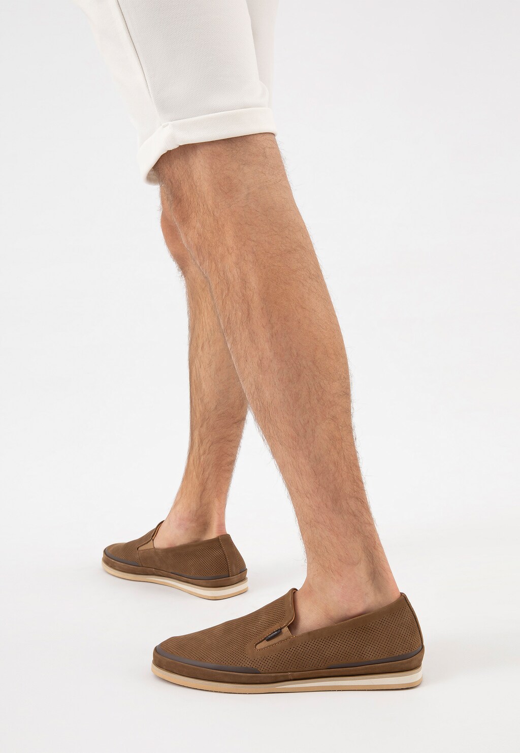 Beżowe wsuwane półbuty męskie Wojas model 10113-24 z nubuku prezentowane na nogach mężczyzny w białych spodniach, widok z boku ukazujący perforowaną cholewkę i jasną podeszwę.