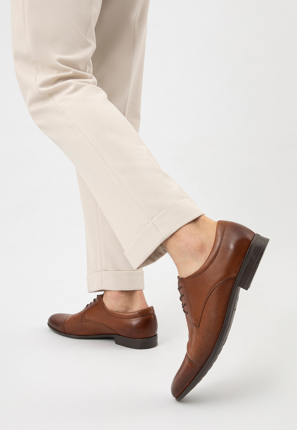 Eleganckie brązowe półbuty męskie Wojas model 10140-52 na nodze w jasnych spodniach, widok z tyłu pokazujący perforowany wzór na skórze i klasyczny profil obuwia.