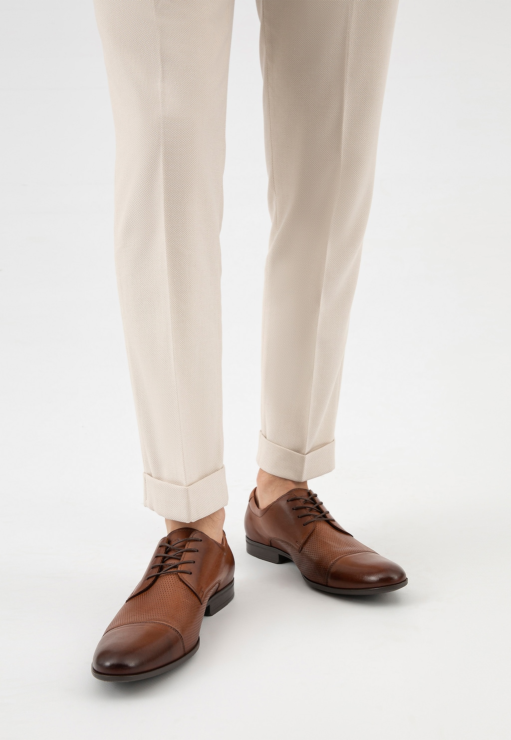 Eleganckie brązowe półbuty Wojas model 10140-52 noszone ze stylowymi jasnymi spodniami. Widok z przodu na buty ze skórzanym ażurowym wykończeniem i sznurowaniem.