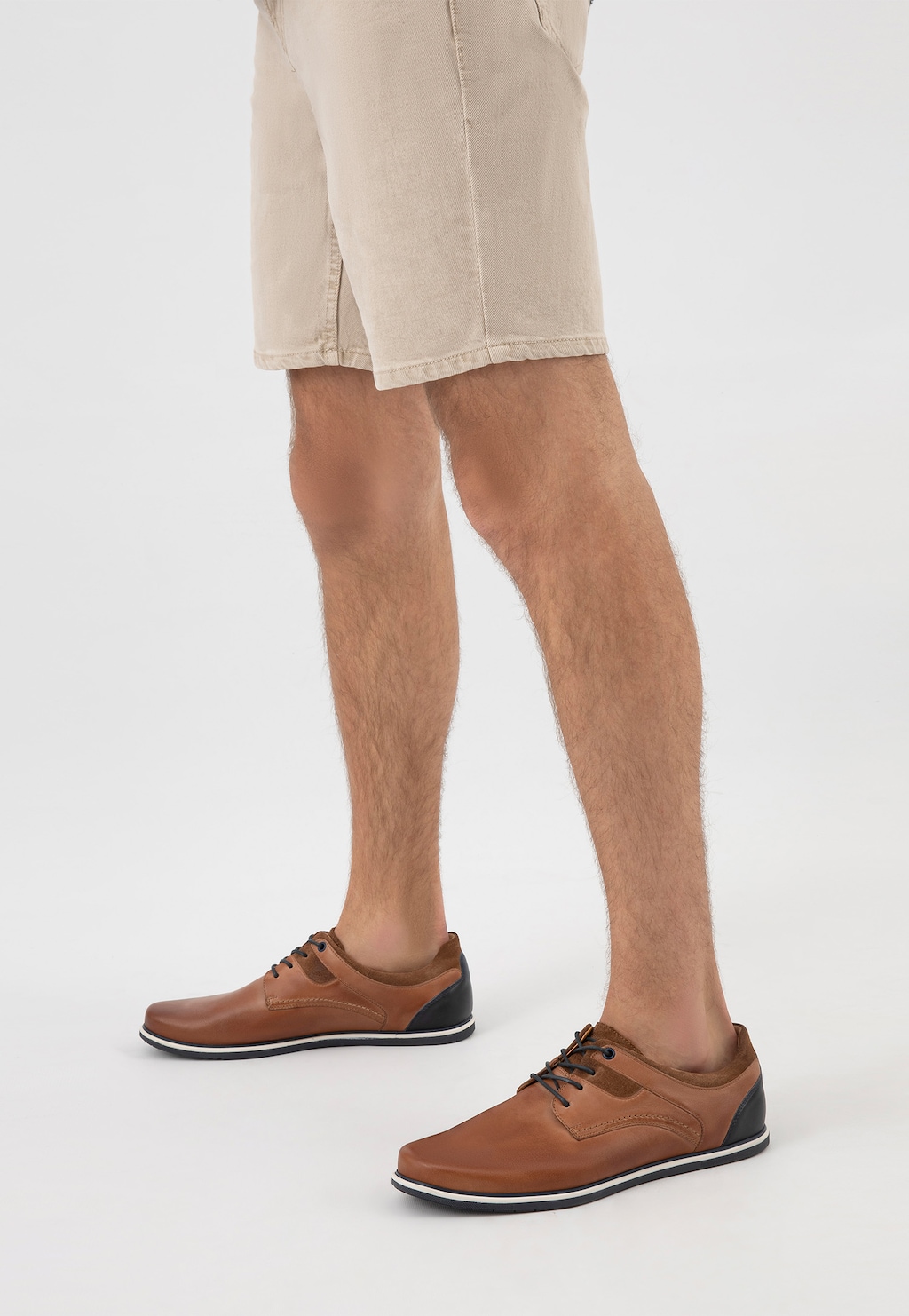 Eleganckie brązowe półbuty męskie Wojas model 10027-73 z granatową wstawką na pięcie, prezentowane na nogach modela ubranego w beżowe szorty.