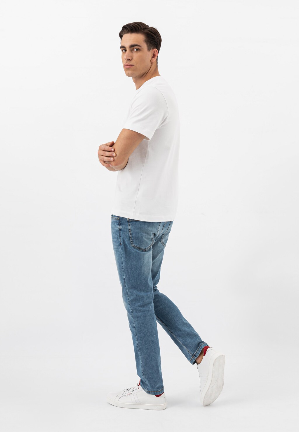 Model w białym t-shircie i jeansach prezentuje białe skórzane trampki męskie Wojas model 10167-50 z czerwonymi wstawkami, widocznymi przy stopie.