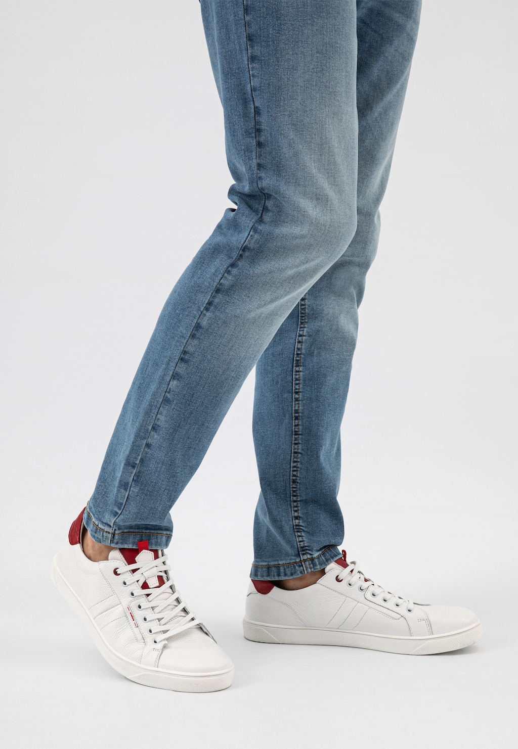 Białe skórzane trampki męskie Wojas model 10167-50 z czerwonymi wstawkami na pięcie, noszone do jasnoniebieskich jeansów, widok z boku.
