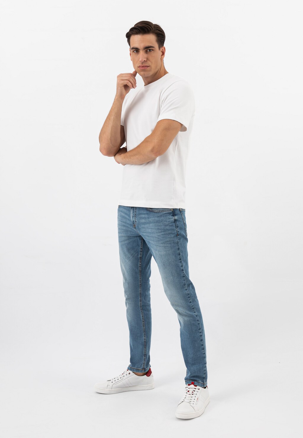 Model w białej koszulce i niebieskich jeansach prezentuje białe skórzane trampki męskie Wojas 10167-50 z charakterystycznymi czerwonymi wstawkami.