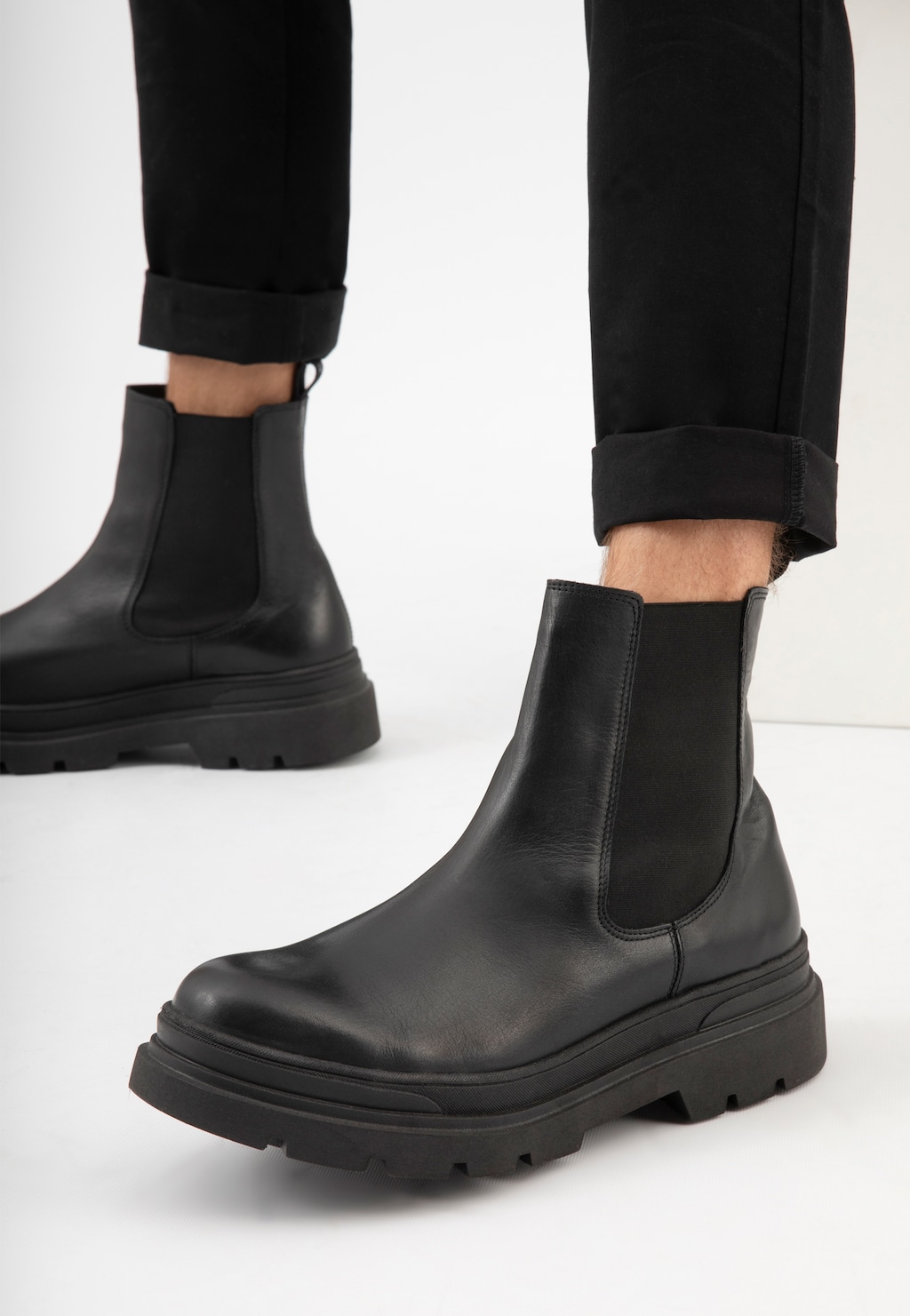 Czarne sztyblety męskie Wojas model 20013-51 z grubą podeszwą, widoczne na nogach w czarnych spodniach. Buty ze skóry z elastycznymi wstawkami po bokach.