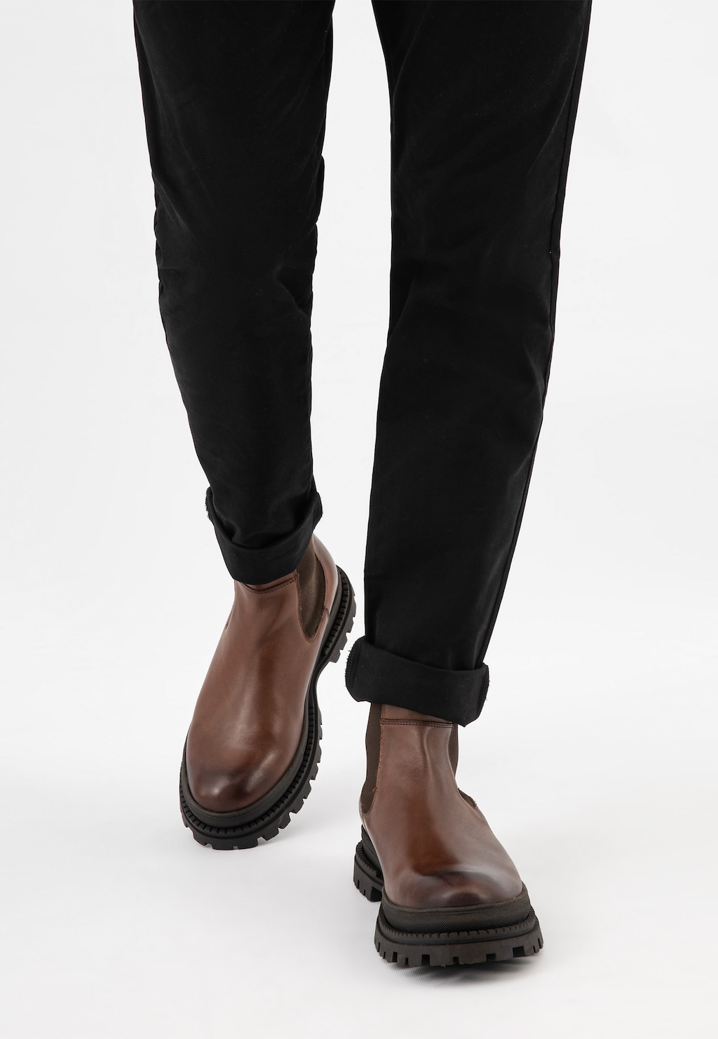 Eleganckie brązowe sztyblety męskie Wojas 20018-52 z grubą podeszwą, noszone z czarnymi spodniami. Widok z przodu na nogi modela prezentującego skórzane buty o masywnym designie.