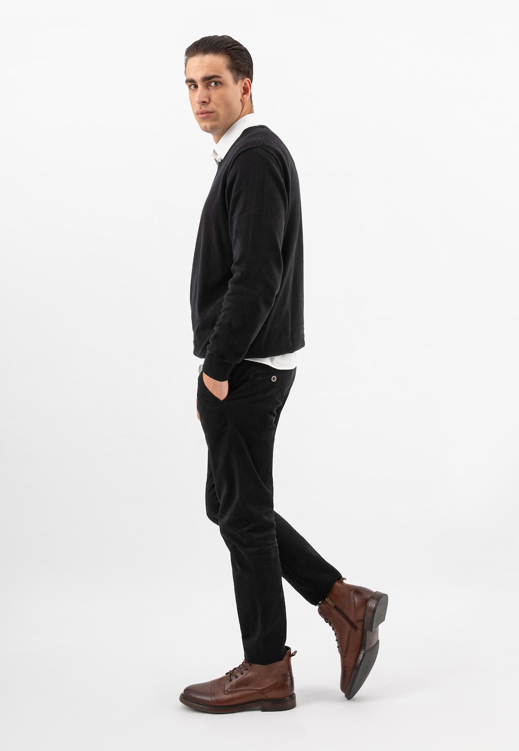 Model w eleganckim stroju prezentuje klasyczne brązowe trzewiki męskie Wojas model 24035-52, idealnie pasujące do czarnego swetra i spodni.