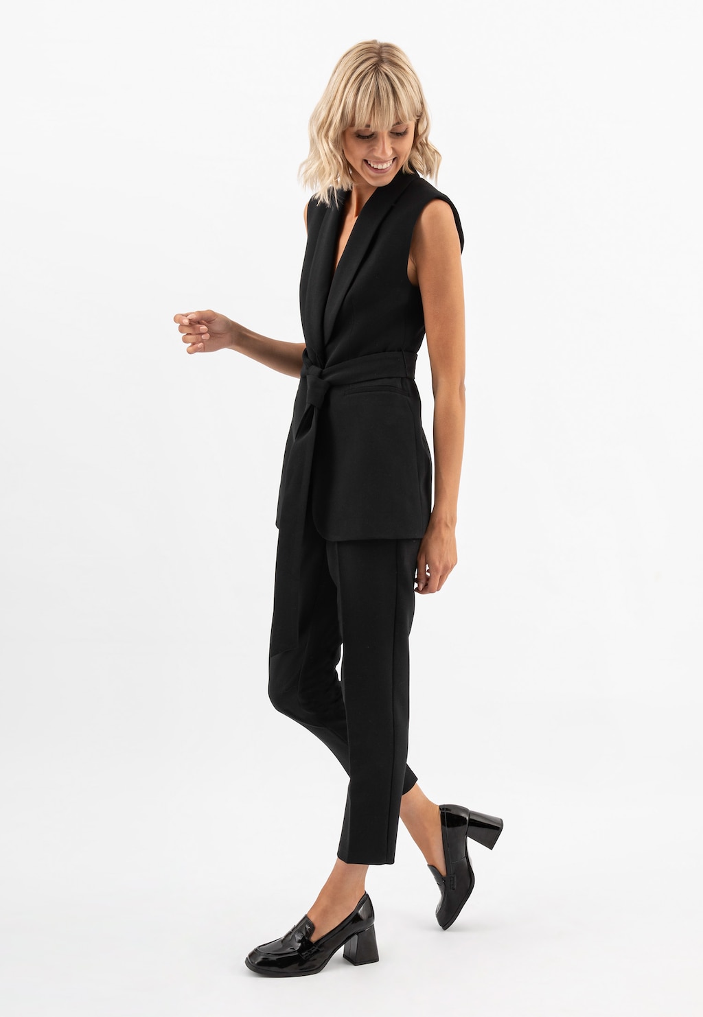 Kobieta w eleganckim czarnym komplecie prezentuje czarne lakierowane mokasyny damskie Wojas 46204-31 na solidnym obcasie, idealne uzupełnienie biznesowej stylizacji.